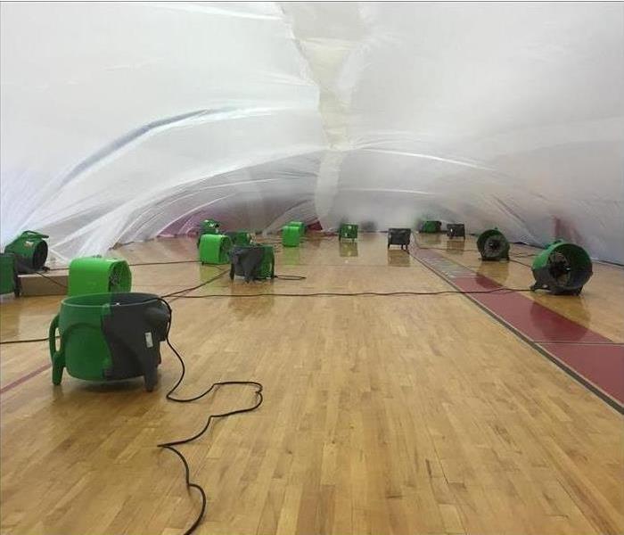 Plastic over a basketball gym floor with equipment under it.