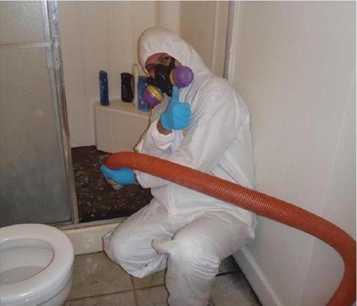 Person in tyvek suit and mask extracting sewage backed up in a shower